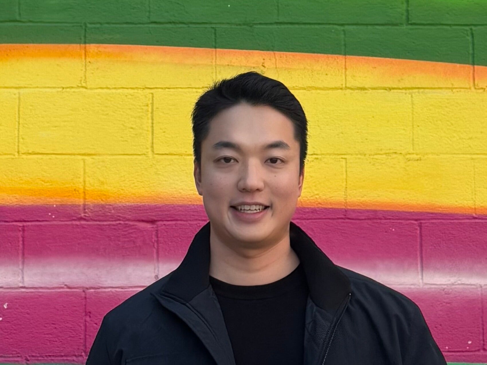 Jee Hoon Kim smiling in front of painted brick wall.
