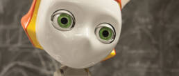 image of robot staring into distance. robot has white face green eyes and orange hair