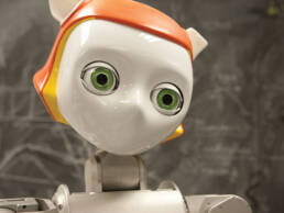 image of robot staring into distance. robot has white face green eyes and orange hair