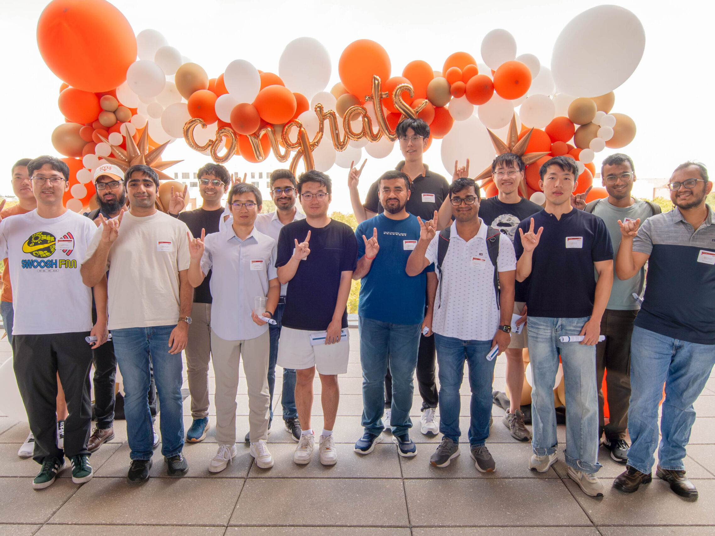 Student winners of Amazon AI Fellowships stand in front of balloons doing Hook Em to camera.