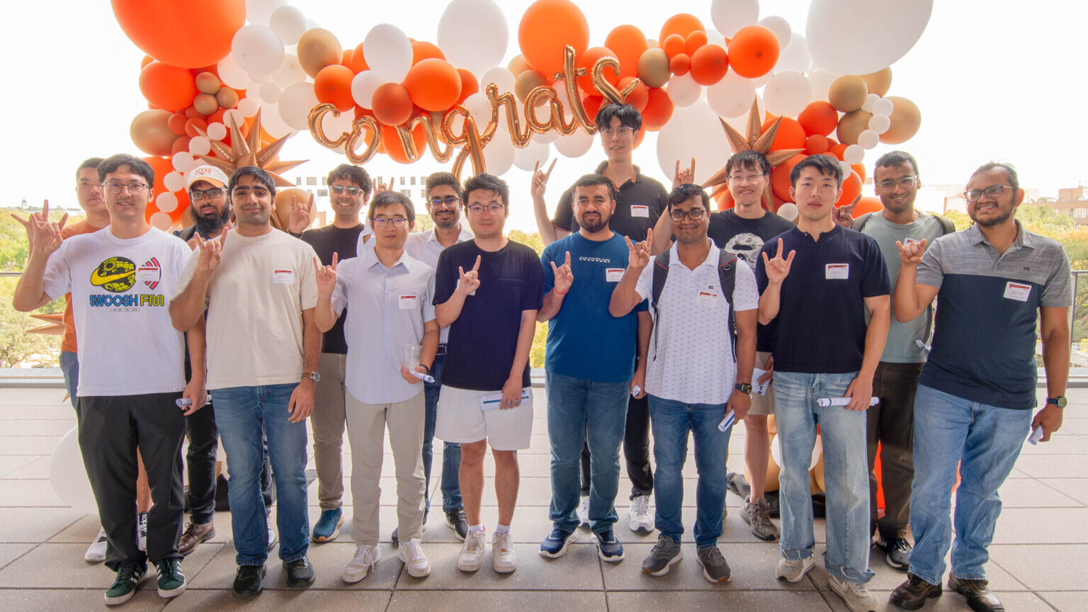 Student winners of Amazon AI Fellowships stand in front of balloons doing Hook Em to camera.