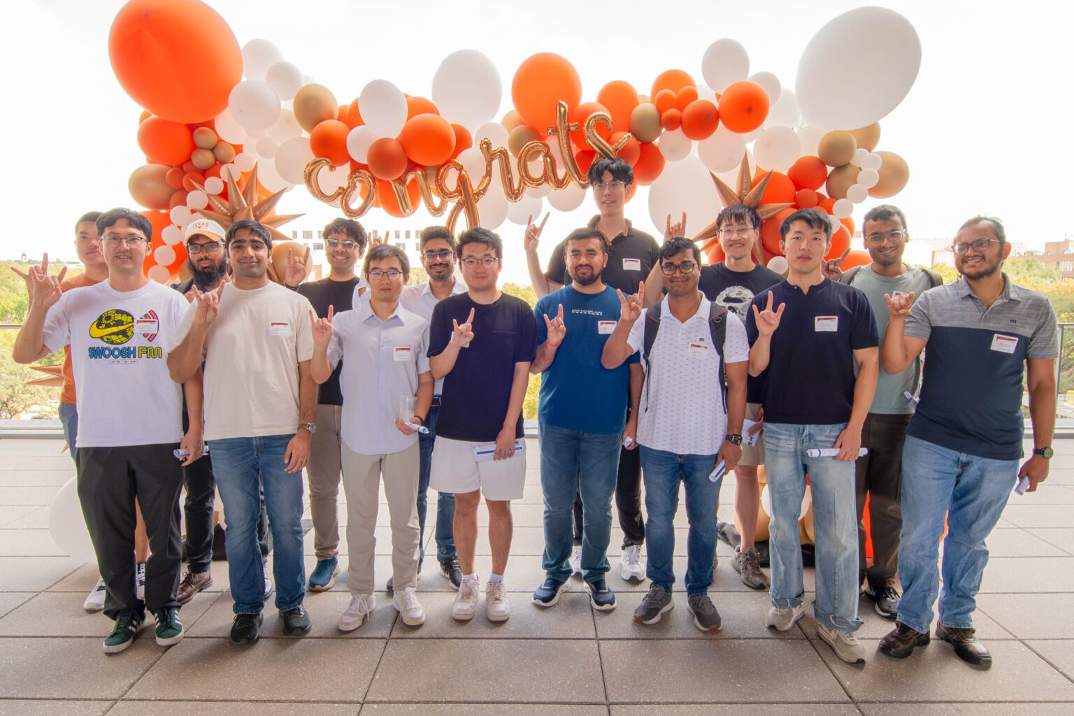 Student winners of Amazon AI Fellowships stand in front of balloons doing Hook Em to camera.