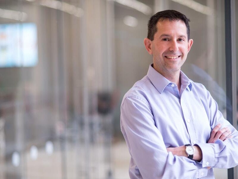 Peter Stone smiling with arms crossed in front of glass room.